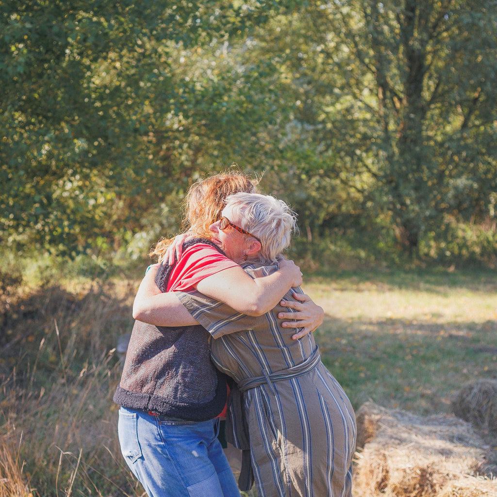 Two people hugging in a field with trees in the background